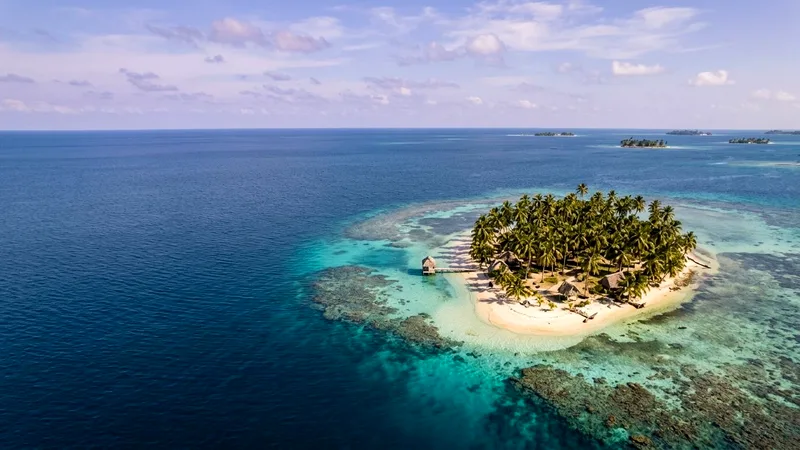 Small palm-covered San Blas island surrounded by turquoise water and coral reef.